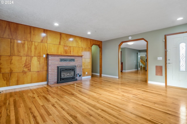 unfurnished living room with light wood-type flooring, a textured ceiling, and wooden walls