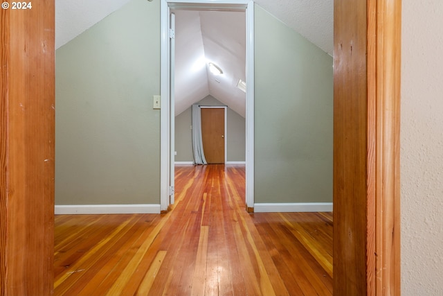 hall featuring a textured ceiling, hardwood / wood-style flooring, and lofted ceiling