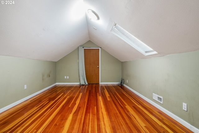 additional living space with vaulted ceiling with skylight and wood-type flooring