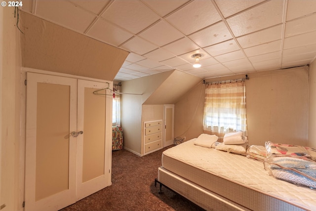 bedroom with a drop ceiling, multiple windows, and dark colored carpet