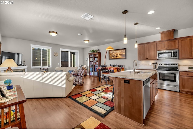 kitchen featuring sink, stainless steel appliances, light stone counters, light hardwood / wood-style flooring, and pendant lighting