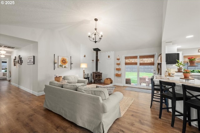 living area with baseboards, visible vents, wood finished floors, a wood stove, and vaulted ceiling