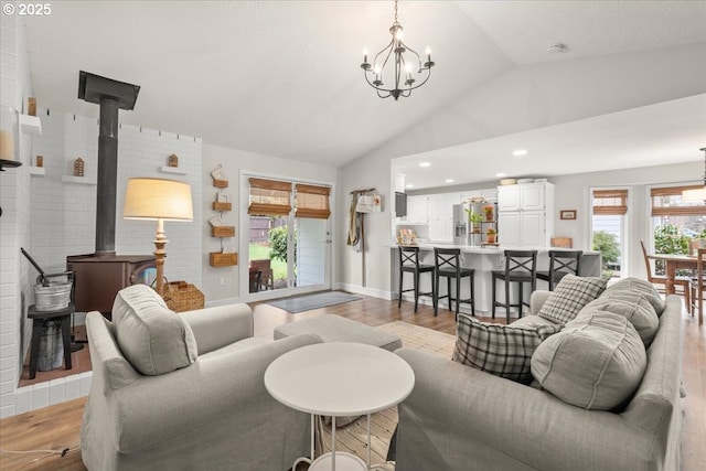 living area featuring a wood stove, light wood-style floors, a wealth of natural light, and lofted ceiling