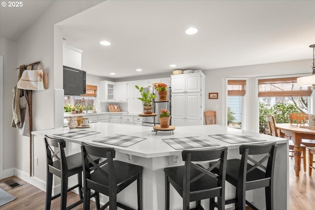 kitchen with light countertops, hanging light fixtures, white cabinets, light wood-type flooring, and a kitchen breakfast bar