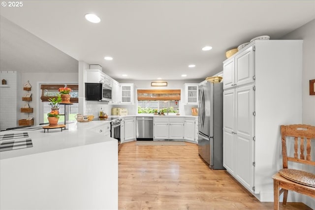 kitchen with light countertops, appliances with stainless steel finishes, glass insert cabinets, white cabinets, and light wood-type flooring