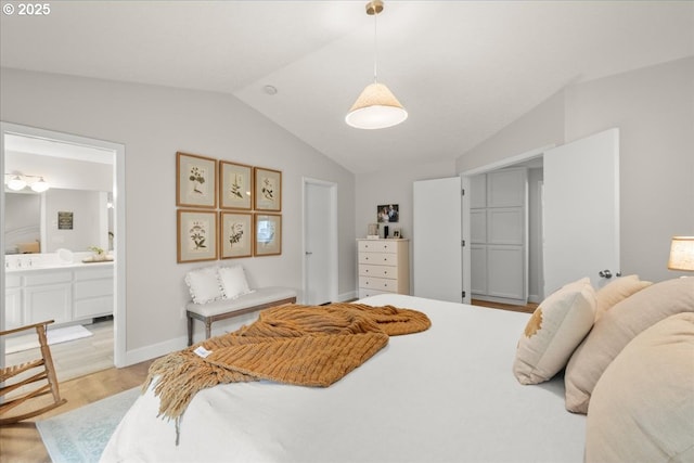 bedroom featuring light wood-style floors, baseboards, vaulted ceiling, and connected bathroom