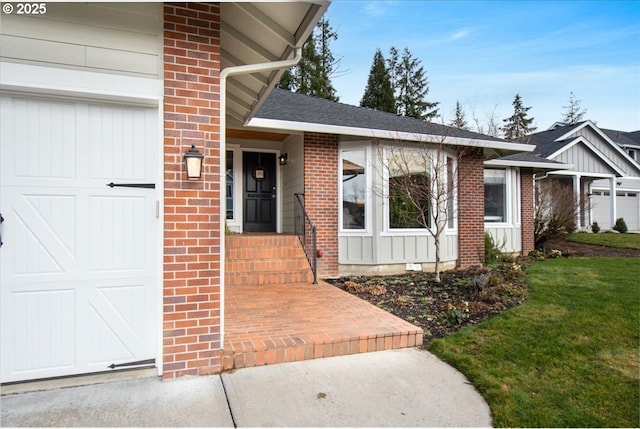 view of exterior entry with a garage, a shingled roof, a yard, board and batten siding, and brick siding