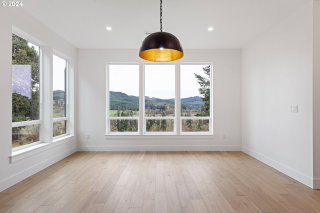 unfurnished dining area featuring a mountain view, a healthy amount of sunlight, and light hardwood / wood-style flooring