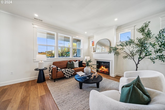 living area with a healthy amount of sunlight, wood finished floors, visible vents, and crown molding