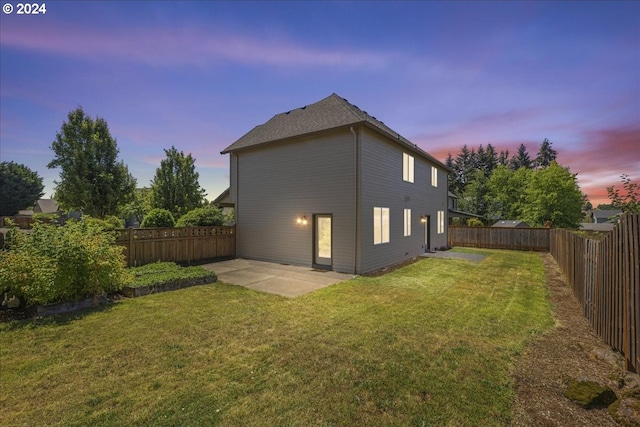 back house at dusk with a patio and a lawn