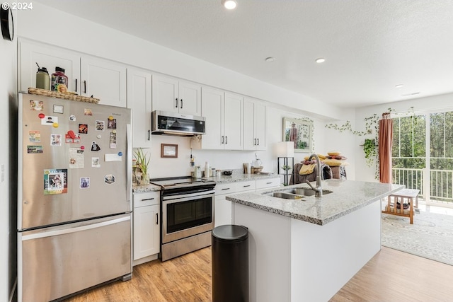 kitchen with white cabinets, appliances with stainless steel finishes, an island with sink, sink, and light stone counters