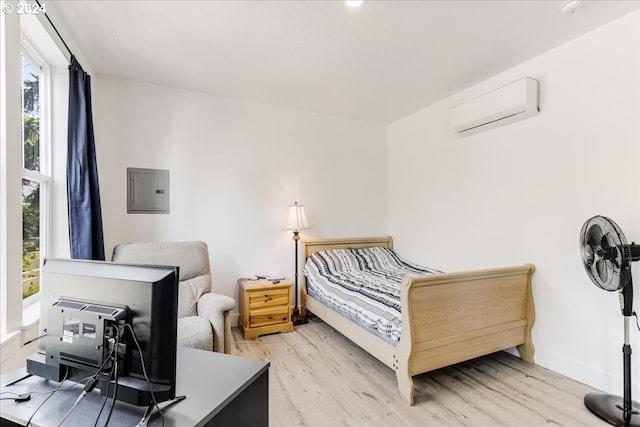 bedroom featuring electric panel, light hardwood / wood-style flooring, and a wall mounted air conditioner