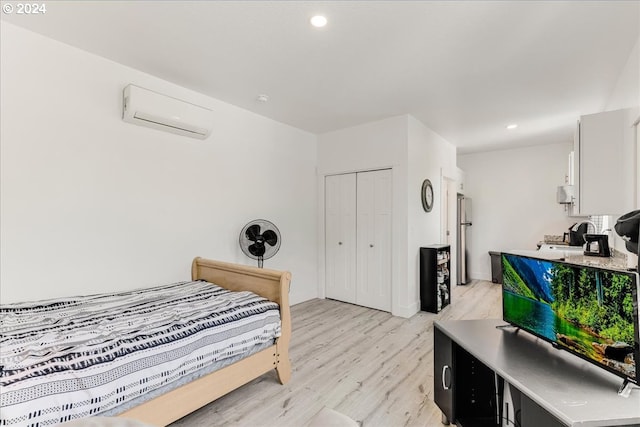 bedroom featuring a wall unit AC, a closet, light hardwood / wood-style flooring, and stainless steel fridge