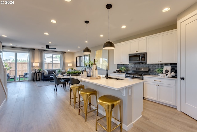 kitchen featuring stainless steel gas range oven, open floor plan, decorative backsplash, light wood-style floors, and a sink