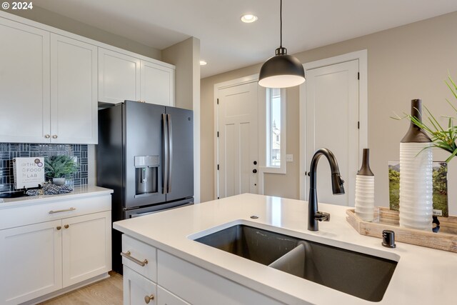 kitchen with hanging light fixtures, light countertops, stainless steel refrigerator with ice dispenser, and a sink