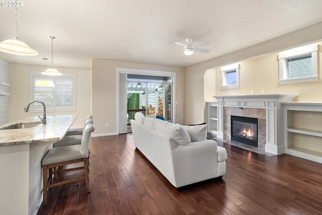 living room with a tiled fireplace, ceiling fan, sink, and dark hardwood / wood-style floors