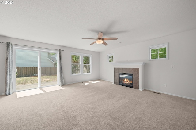 unfurnished living room featuring ceiling fan, a textured ceiling, a tile fireplace, and light colored carpet