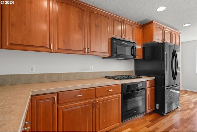 kitchen featuring black appliances, light wood-type flooring, and a textured ceiling