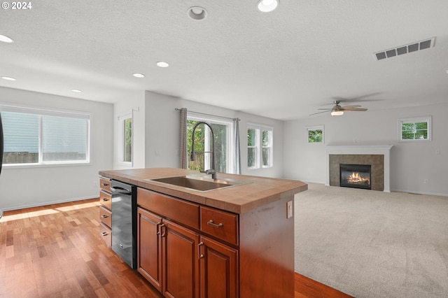 kitchen featuring a center island with sink, a fireplace, ceiling fan, sink, and light colored carpet