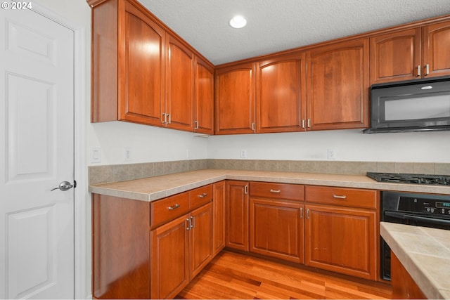 kitchen with tile countertops, a textured ceiling, black appliances, and light hardwood / wood-style floors