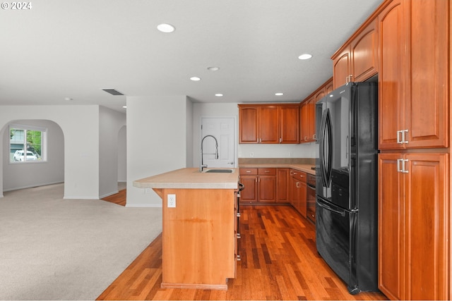 kitchen with an island with sink, black fridge, light carpet, and sink