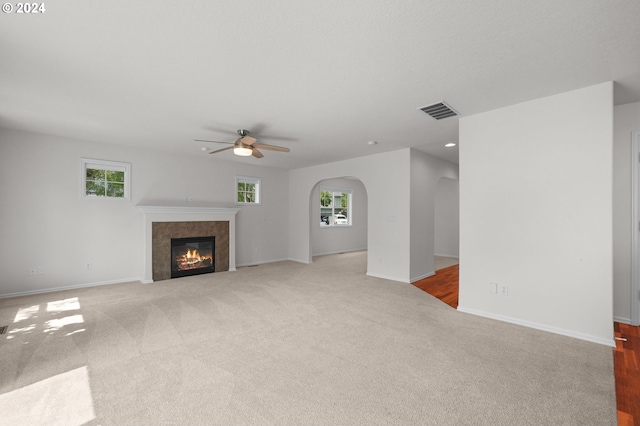 unfurnished living room with a tile fireplace, ceiling fan, and carpet floors