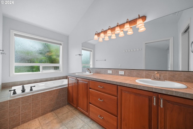 bathroom featuring plenty of natural light, tiled bath, vaulted ceiling, and dual vanity