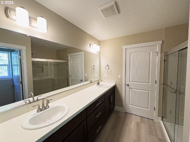 bathroom featuring walk in shower, vanity with extensive cabinet space, hardwood / wood-style floors, dual sinks, and a textured ceiling