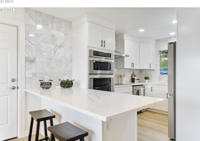 kitchen featuring white cabinetry, stainless steel appliances, light hardwood / wood-style flooring, kitchen peninsula, and a breakfast bar area