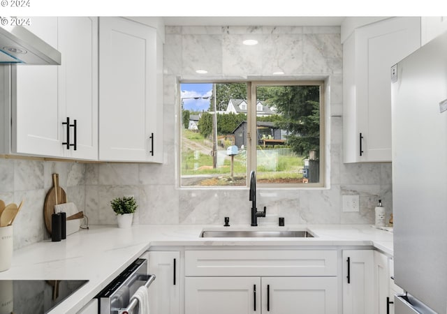 kitchen with light stone counters, stainless steel appliances, exhaust hood, sink, and white cabinets