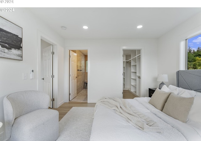 bedroom with light hardwood / wood-style floors, a spacious closet, connected bathroom, and a closet