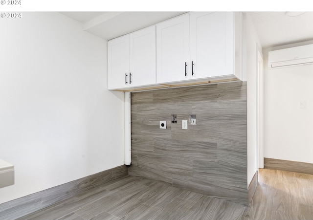 clothes washing area featuring a wall unit AC, hardwood / wood-style floors, electric dryer hookup, and cabinets