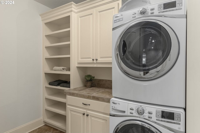 laundry area featuring stacked washer and clothes dryer, cabinets, and dark tile patterned flooring