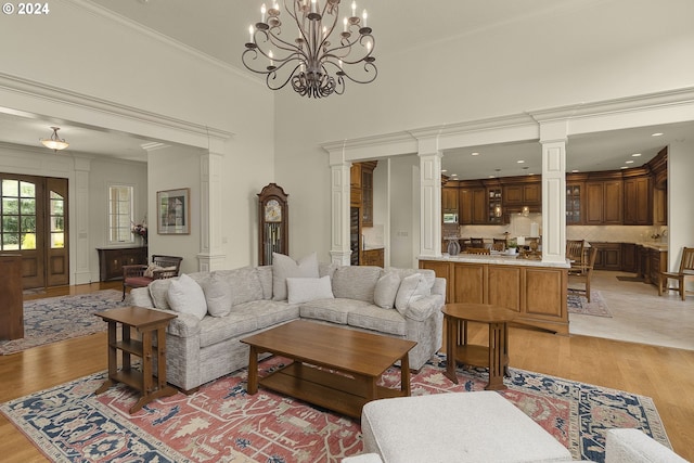 living room featuring light hardwood / wood-style floors, an inviting chandelier, crown molding, and decorative columns