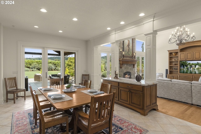 tiled dining space with a stone fireplace, ornate columns, a notable chandelier, ornamental molding, and a textured ceiling