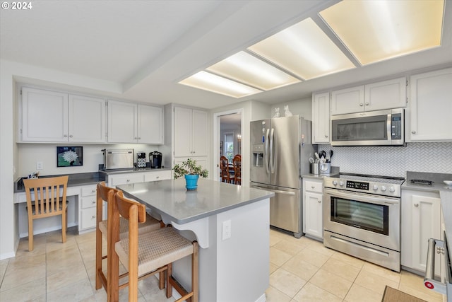 kitchen featuring backsplash, a breakfast bar, stainless steel appliances, a center island, and white cabinetry