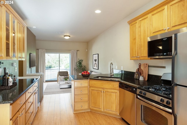 kitchen with light brown cabinets, stainless steel appliances, dark stone countertops, sink, and light wood-type flooring