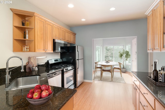 kitchen featuring light wood-type flooring, light brown cabinetry, appliances with stainless steel finishes, sink, and dark stone counters