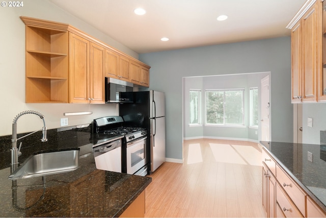 kitchen featuring light hardwood / wood-style flooring, stainless steel appliances, dark stone countertops, light brown cabinetry, and sink