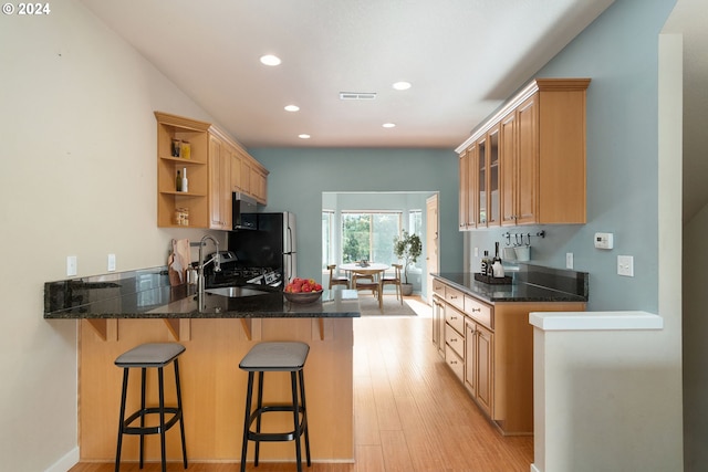 kitchen with kitchen peninsula, light hardwood / wood-style flooring, dark stone counters, and sink