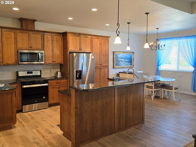 kitchen with pendant lighting, stainless steel appliances, and a kitchen island with sink