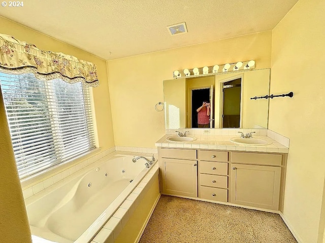 bathroom featuring vanity, a textured ceiling, and tiled bath