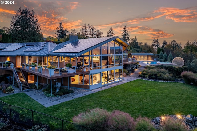 back house at dusk featuring a sunroom, a swimming pool side deck, and a yard