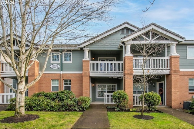 view of front of home with a front yard, a balcony, and central AC