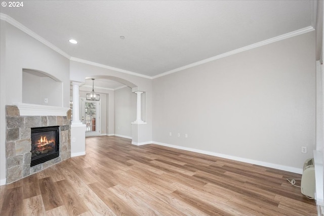 unfurnished living room with decorative columns, a stone fireplace, crown molding, and light hardwood / wood-style flooring