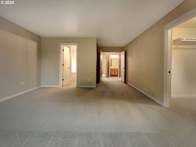 unfurnished bedroom featuring connected bathroom, a walk in closet, and light colored carpet