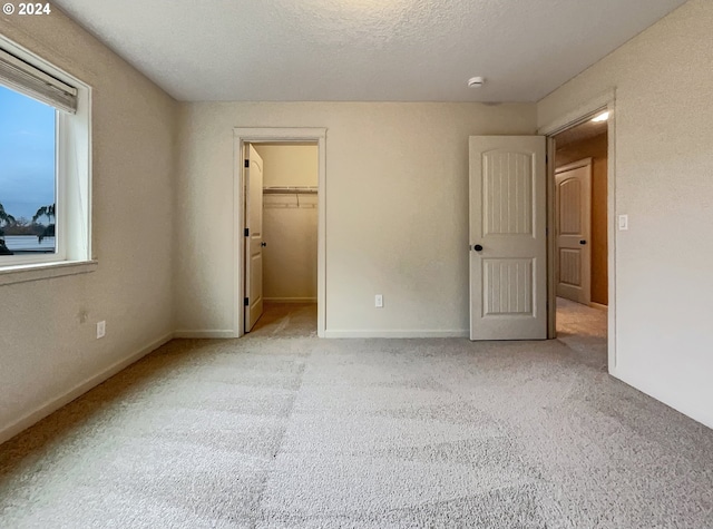 unfurnished bedroom featuring light colored carpet, a walk in closet, a textured ceiling, and a closet