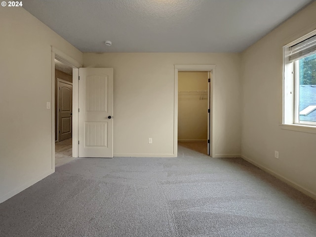 unfurnished bedroom featuring light colored carpet, a spacious closet, a textured ceiling, and a closet