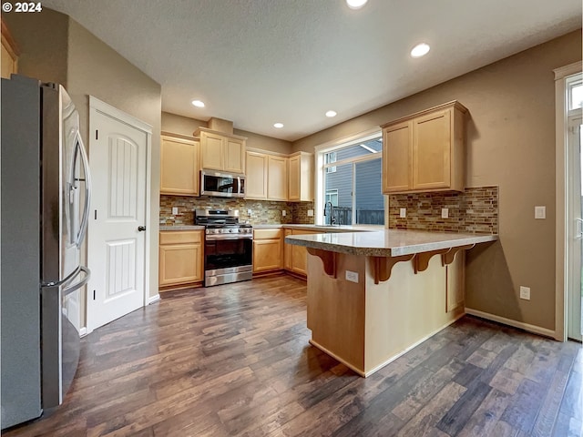 kitchen with a kitchen breakfast bar, sink, dark hardwood / wood-style floors, kitchen peninsula, and stainless steel appliances