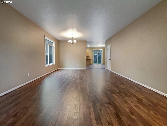 unfurnished living room with dark hardwood / wood-style flooring, a textured ceiling, and a notable chandelier